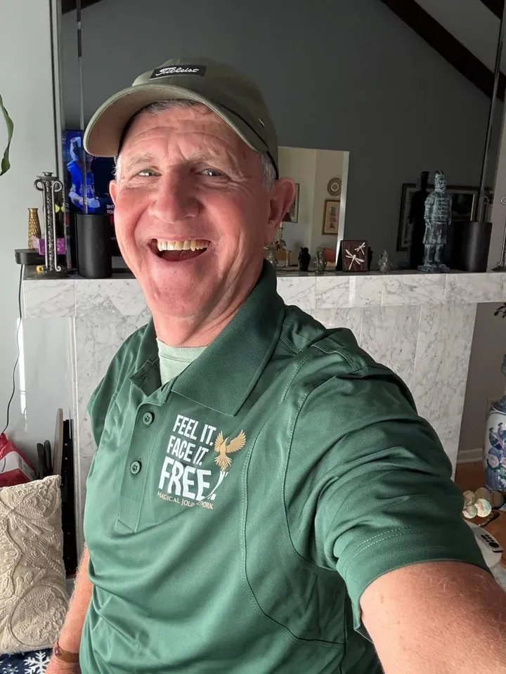 Magic smiling in a green shirt with a gold phoenix that reads Feel it. Face it. Free.